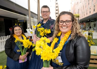 Three people hold daffodils to celebrate Daffodil Day in Adelaide's Rundle Mall in August 2026.