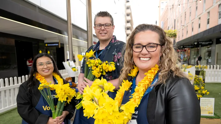 Three people hold daffodils to celebrate Daffodil Day in Adelaide's Rundle Mall in August 2026.