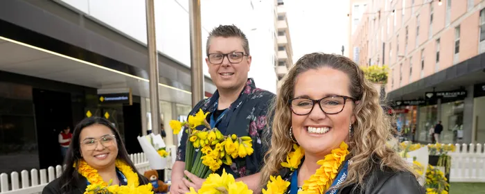Three people hold daffodils to celebrate Daffodil Day in Adelaide's Rundle Mall in August 2026.