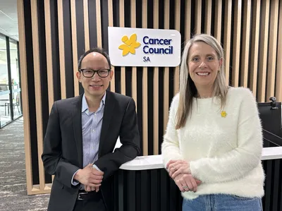 A man and a woman stand in front of a Cancer Council SA sign