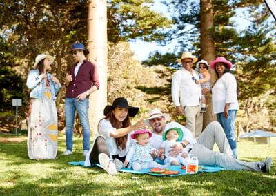 Six adults and three young children practice sun safe behaviours in the shade in a park