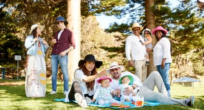 Six adults and three young children practice sun safe behaviours in the shade in a park