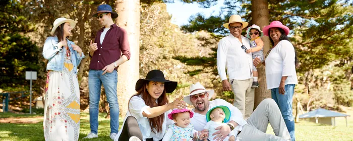 Six adults and three young children practice sun safe behaviours in the shade in a park