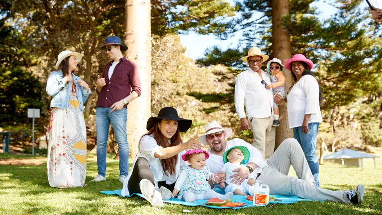 Six adults and three young children practice sun safe behaviours in the shade in a park