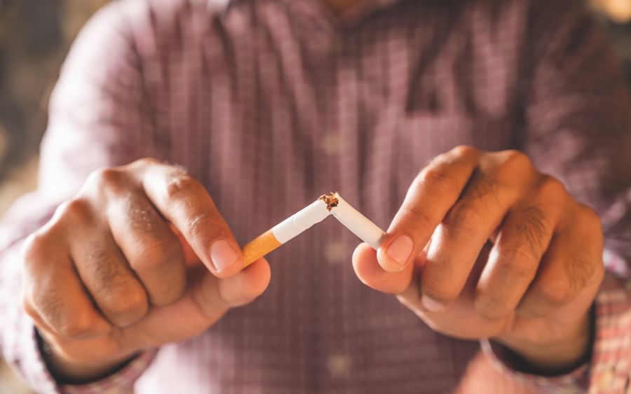 Person in a checkered shirt breaks a cigarette in half, ash at the broken end.