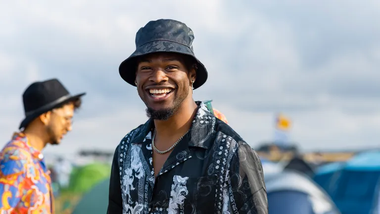 Smiling person in a black patterned shirt and bucket hat at an outdoor event.